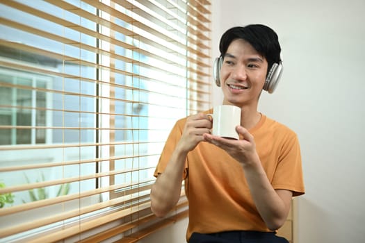 Portrait of positive man in wireless headphone drinking coffee and looking away.