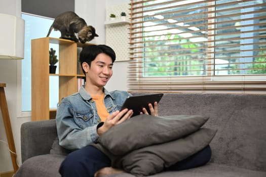 Shot of smiling man watching video using digital tablet and relaxing on couch in living room.