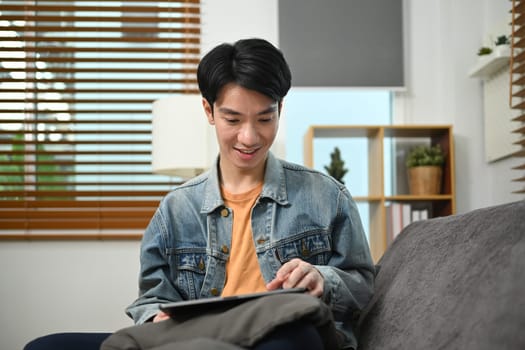 Attractive man relaxing on couch in living room and using digital tablet for internet surfing.