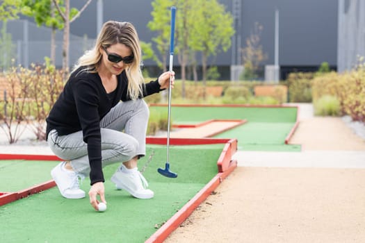 Woman playing mini golf and trying putting ball into hole. Summer leisure activity. High quality photo