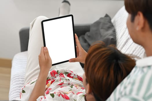 Loving young gay couple using digital tablet while sitting on a couch at home.