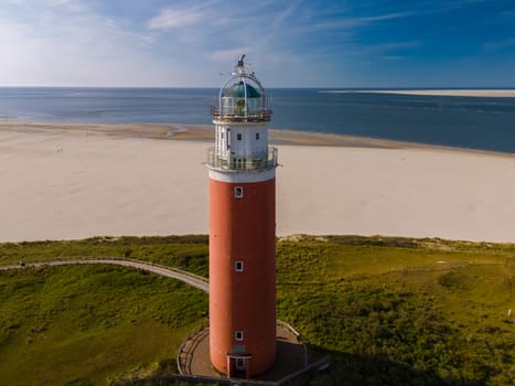 An aerial perspective of a majestic lighthouse standing proudly on the sandy shores of Texel, Netherlands, overlooking the vast expanse of the ocean. The iconic red lighthouse of Texel Netherlands