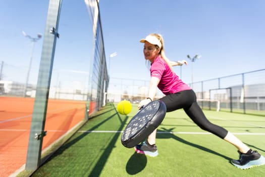 Active young woman trying to beat the ball by Padel racket while playing tennis in the court. High quality photo