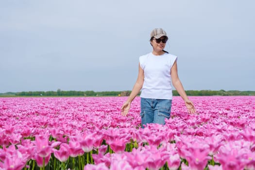 A woman stands in a field of vibrant pink tulips in Texel, Netherlands, surrounded by the beauty of nature.