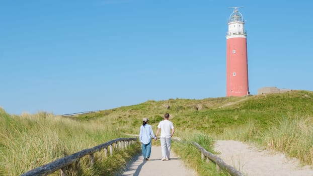 A couple leisurely walks along a scenic path near a historic lighthouse in Texel, Netherlands.