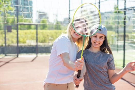 Mother and daughter are playing badminton outside in the yard on summer hot day. High quality photo