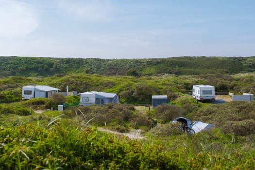 A serene scene of multiple RVs parked in a lush grassy area on the picturesque island of Texel, creating a cozy camping community under the open sky.