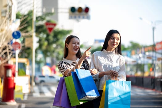 Two young women are seen enjoying a shopping day out in the city, holding colorful shopping bags and sharing smiles.