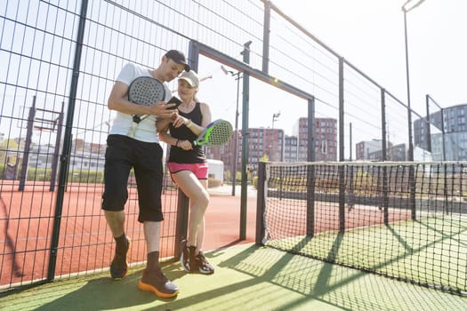 Cheerful athletic couple laughing during padel tennis match on outdoor court. High quality photo