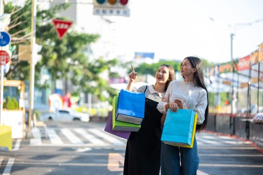 Two young women are seen enjoying a shopping day out in the city, holding colorful shopping bags and sharing smiles.