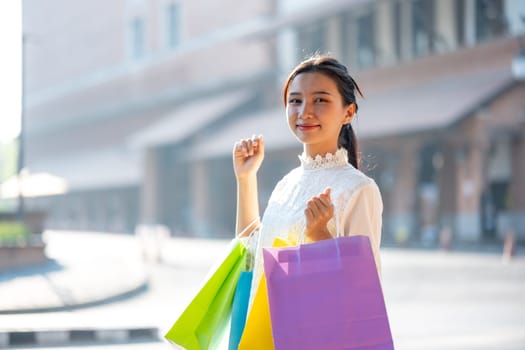 Cheerful young woman enjoying a shopping spree, holding colorful shopping bags in a sunny outdoor setting.