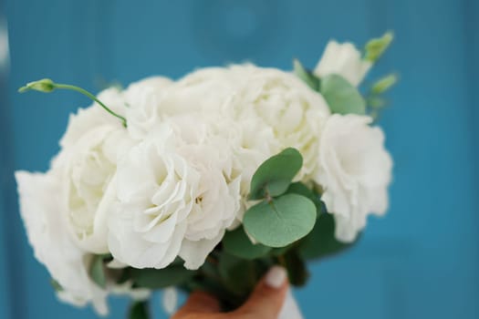 A bouquet of white flowers is being held by a person. The flowers are arranged in a vase and are placed on a blue background. The bouquet has a simple and elegant design