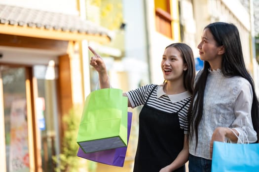 Two young women are seen enjoying a shopping day out in the city, holding colorful shopping bags and sharing smiles.