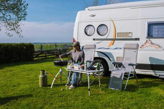 A woman sits at a table next to an RV in Texel, Netherlands, enjoying the peace and quiet of the countryside.