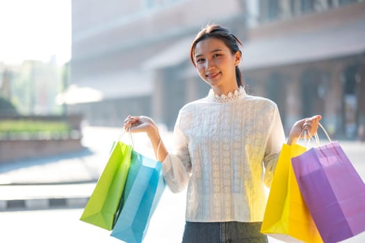 Cheerful young woman enjoying a shopping spree, holding colorful shopping bags in a sunny outdoor setting.