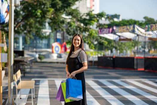 Cheerful young woman enjoying a shopping spree, holding colorful shopping bags in a sunny outdoor setting.