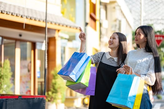 Two young women are seen enjoying a shopping day out in the city, holding colorful shopping bags and sharing smiles.
