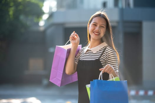 Cheerful young woman enjoying a shopping spree, holding colorful shopping bags in a sunny outdoor setting.