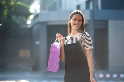 Cheerful young woman enjoying a shopping spree, holding colorful shopping bags in a sunny outdoor setting.