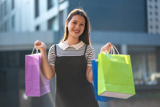 Cheerful young woman enjoying a shopping spree, holding colorful shopping bags in a sunny outdoor setting.