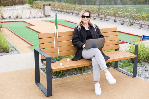 Woman using a laptop and mobile phone on the golf course. High quality photo