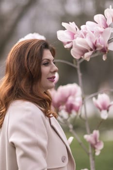 Woman magnolia flowers, surrounded by blossoming trees, hair down, wearing a light coat. Captured during spring, showcasing natural beauty and seasonal change