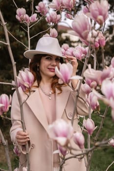 Woman magnolia flowers, surrounded by blossoming trees, hair down, white hat, wearing a light coat. Captured during spring, showcasing natural beauty and seasonal change