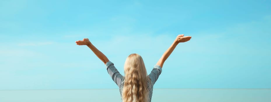 Summer vacation, happy young woman raising her hands up on the beach on sea coast and blue sky background