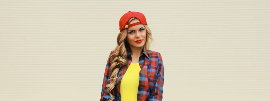 Portrait of stylish young blonde woman in red baseball cap posing against white wall background