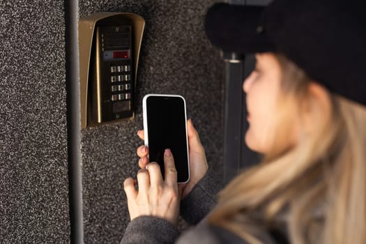 Female hand holding black mobile smart phone with smart home application on the screen. Blurred house on the background. For access to all of the controls of your house and caring of home security. High quality photo