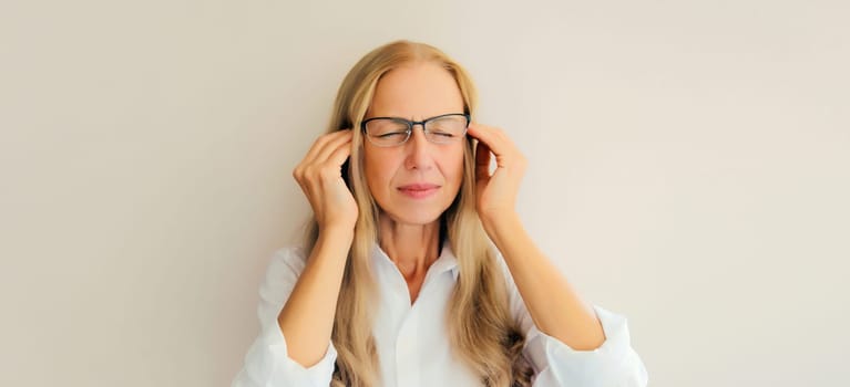 Exhausted tired caucasian mature woman employee with headache, stress, fatigue, temples pain, suffers from migraine, tension in the head in the office