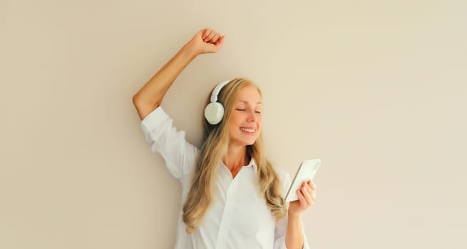 Happy cheerful middle aged woman listening to music with mobile phone in headphones having fun dancing on studio background