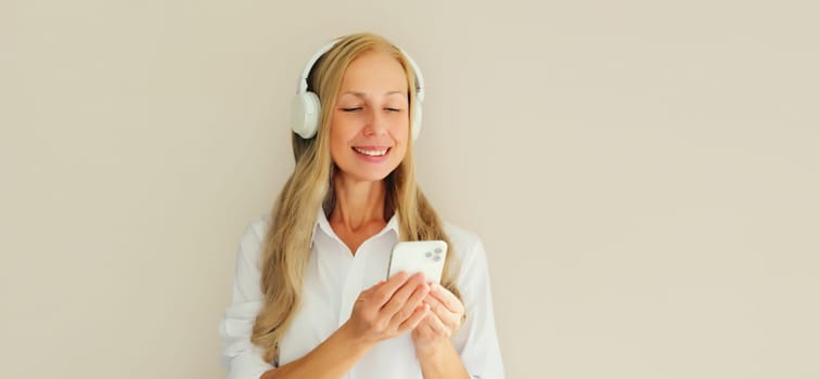 Happy smiling middle aged woman listening to music with mobile phone in headphones on studio background