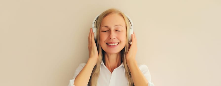 Portrait of happy relaxed middle aged woman listening to music in wireless headphones on white background