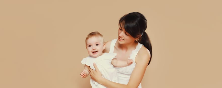 Happy cheerful smiling young mother playing with cute baby on brown studio background