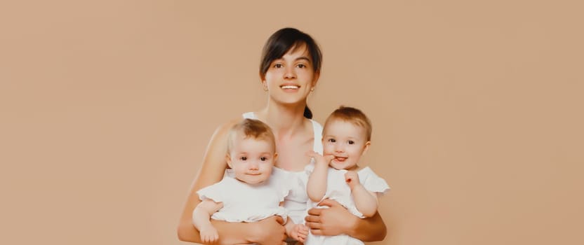 Happy cheerful smiling young mother holding baby on brown studio background