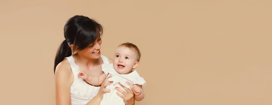 Happy cheerful smiling young mother playing with cute baby on brown studio background