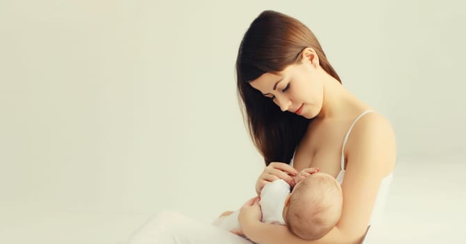 Portrait of happy young mother breastfeeding her baby at home on white background