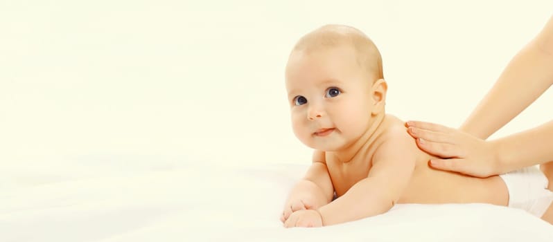 Close up mother gives massage to baby lying on the bed on white background, child and health concept