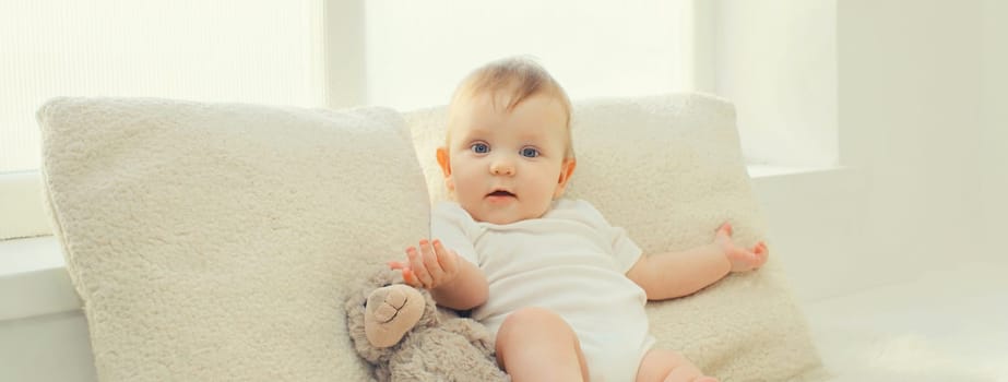 Happy cute little baby playing with teddy bear toy on the floor in white room at home