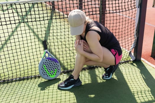 Lose again. Frustrated sexy woman in sportswear sitting near a tennis net.The sportswoman is upset. High quality photo