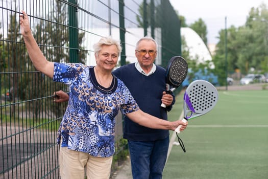 Portrait of sporty fit senior woman playing padel on open court on summer day, ready to hit ball. Health and active lifestyle concept.. High quality photo