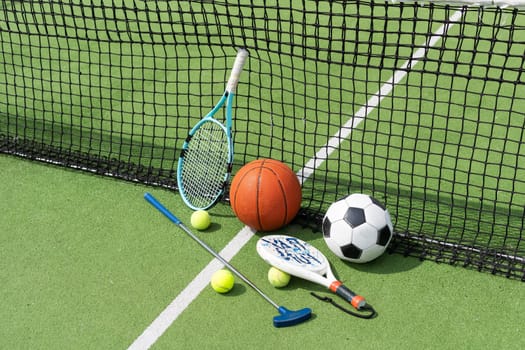 A variety of sports equipment including an american football, a soccer ball, a tennis racket, a tennis ball, and a basketball. High quality photo