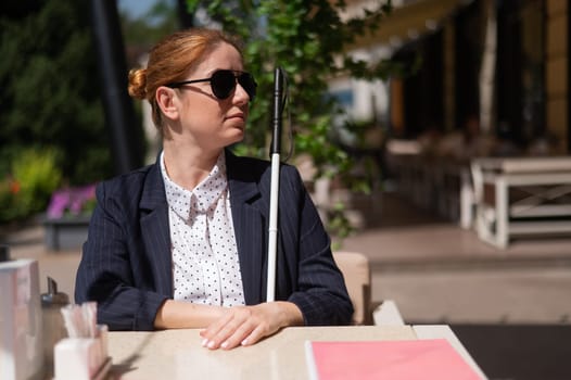 A blind woman in a business suit is sitting in an outdoor cafe