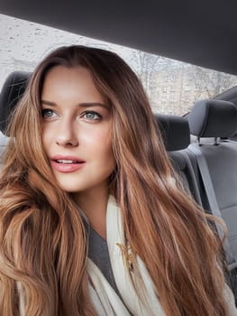 Young woman with long hair, wavy hairstyle in the car or taxi cab as passenger, exploring the city, transport and travel idea