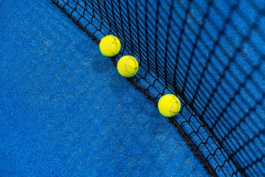 several balls by the net on a blue paddle tennis court. High quality photo