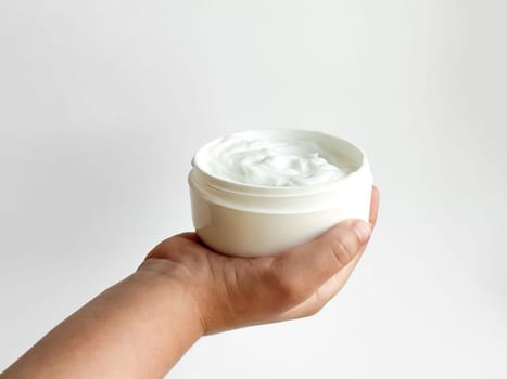 Close up of childs hand holding container of cream on white background with copy space. Skincare and moisturizing concept. Design for healthcare, wellness, and child care poster. High quality photo