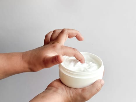 Close up of childs hands holding container of hand cream and dipping finger on white background. Skincare and moisturizing concept. Design for healthcare, wellness, and child care poster. High quality