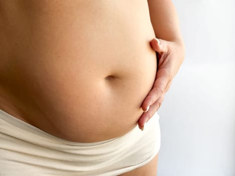 Pregnant belly in beige underwear with hand touching. Close up photography for maternity, pregnancy, and motherhood concept. Design for healthcare, prenatal care and wellness. High quality photo
