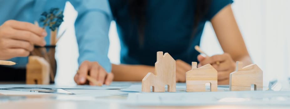 Professional architect engineer team discussion about architectural project on meeting table with wooden block and blueprint scatter around. Design and cooperate concept. Closeup. Delineation.